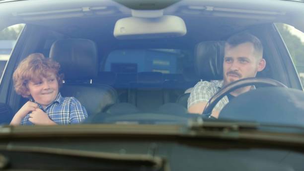 istock Smiling father driving car while his little son sitting next to him. Slow motion 1813302588