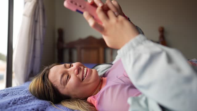 Young woman using phone lying down on bed in the bedroom at hotel room
