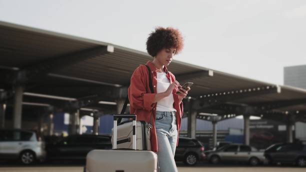 istock Smiling woman with suitcase standing outdoors, holding phone. 1813336722