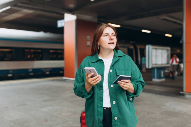 istock Young redhead woman waiting train with backpack and using smart phone. Railroad transport concept, Traveler. 30s Woman with suitcase walking at railroad station platform. Travel to vacation by train 1813385625