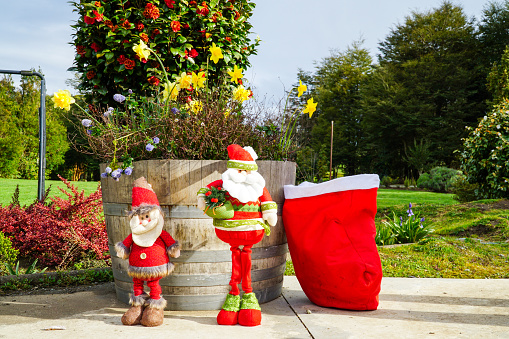 Two mini Santa Claus figurines in the garden of a house.
