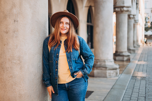 Attractive young female tourist is exploring new city. Redhead girl in hat posing on Market Square in Krakow. Traveling Europe in autumn. High quality photo