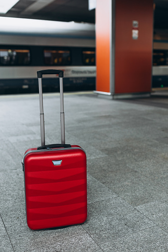 Forgotten travel bag on the train station. Red suitcase on empty station platform. Travel and vacation theme background.