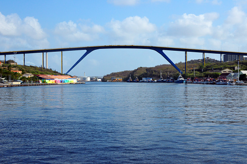 Willemstad, Curaçao, Kingdom of the Netherlands: Queen Juliana Bridge across St. Anna Bay - rigid frame bridge with inclined legs linking Punda to Otrobanda - at 56.4m tall it is the highest bridge in the Caribbean, allowing the passage of most vessels. Building in Otrobanda on the left. Tugs and fishing boats moored along St. Anna Bay, oil refinery in the backgroud.