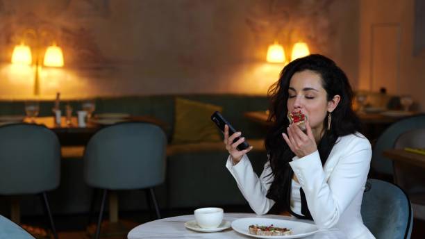istock Young lady sitting in restaurant while biting bruschetta and reading a message, holding mobile phone. Copy space. Business, lifestyle concept. Slow motion 1813411881