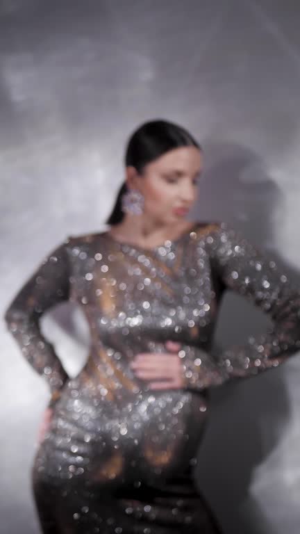 Blur trendy stylish beautiful pregnant woman in a tight silver sequined dress against a white wall background. Vertical