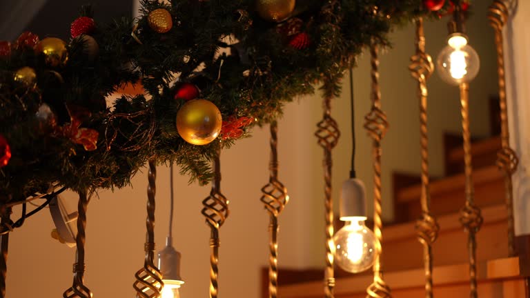 Close-up of a beautifully decorated staircase for Christmas. In the background, out of focus, is the lower torso of a child, in pajamas with a gift in his hands, climbing up the steps of the stairs.