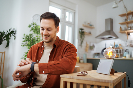 Young smiling casually clothed man using smart watch at home