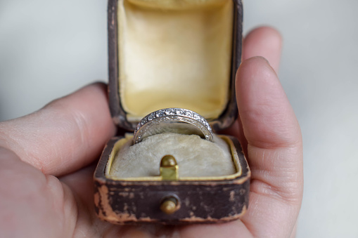 An opened antique / vintage brown leather ring case lined with yellow velvet and silk, with an antique platinum engagement ring with diamonds inside.