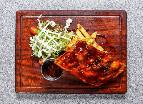 Original bbq pork ribs with French fries and salad served on wooden board isolated on background top view of hong kong food