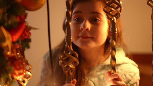Close-up. A girl's look through the wrought-iron balusters of a staircase decorated for Christmas.