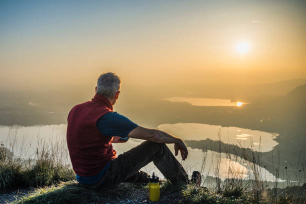 istock Man sitting on a hill looking far the sun 1813489558