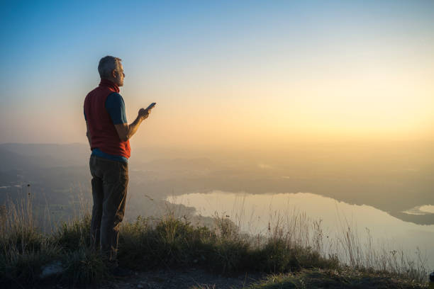 Man standing on a hill checking smartphone, amazing light sunset