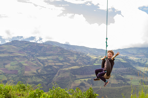 A local backpacker young kid tourist enjoying the landscape view swinging on top of the Pichincha's volcano mountain. On Back, Quito's ecuadorian capital.