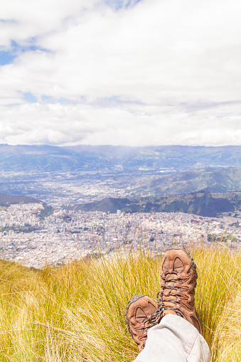 Subjective point of view landscape over the Los Andes Cordillera Highlands. On back, Quito Pichincha, Ecuador.

Part of boots and male legs, sitting over the grass looking Quito's ecuadorian capital.