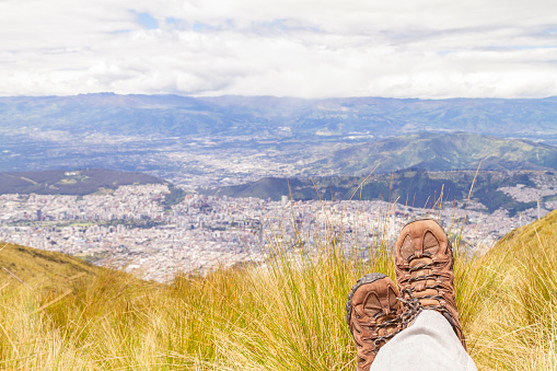 Subjective point of view landscape over the Los Andes Cordillera Highlands. On back, Quito Pichincha, Ecuador.

Part of boots and male legs, sitting over the grass looking Quito's ecuadorian capital.