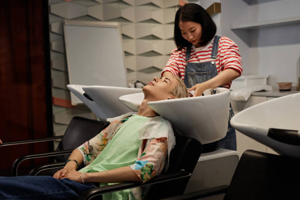 junger asiatischer mann genießt haarwäsche und massage im schönheitssalon - lightener stock-fotos und bilder
