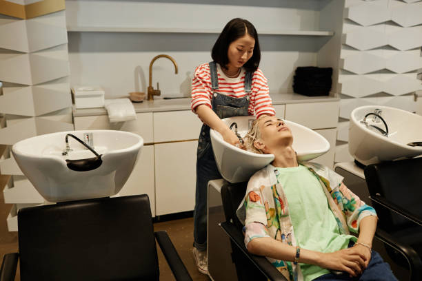 joven asiático disfrutando del cuidado del cabello y del lavado en el fregadero del salón de belleza - lightener fotografías e imágenes de stock