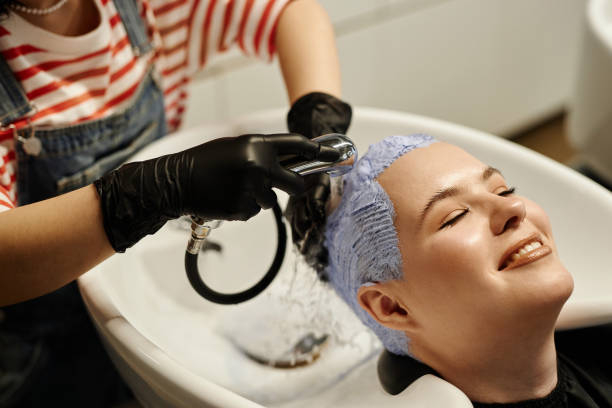 mujer joven sonriente disfrutando del lavado del cabello en el fregadero del salón después de la decoloración - lightener fotografías e imágenes de stock