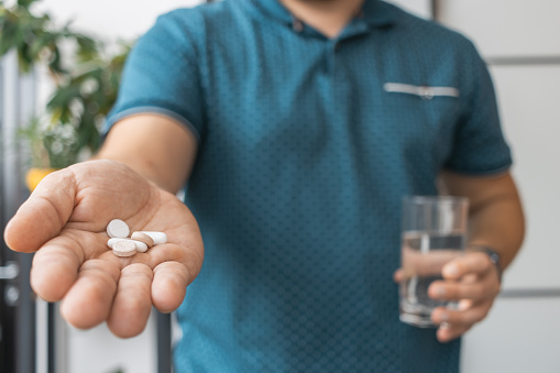 Man taking medicine, holding in a hand various therapeutic pills, antibiotics, painkiller and glass of water, close-up view.