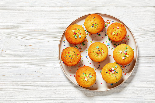 delicious sweet lemon muffins topped with holiday sprinkles on plate on white wooden table, horizontal view from above, flat lay, close-up