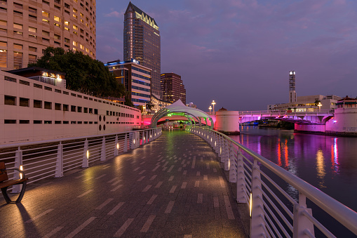 Tampa, Florida, USA - September 23, 2022:  A wide-angle view of Tampa Riverwalk, winding along side of Hillsborough River and with Kennedy Boulevard Bridge in background, on a calm Summer evening.