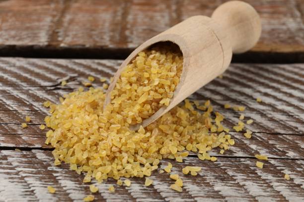 istock Scoop with raw bulgur on wooden table, closeup 1813639504