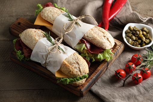 Delicious sandwiches with bresaola, lettuce and other products on wooden table