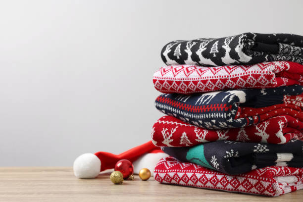 istock Stack of different Christmas sweaters, Santa hat and baubles on wooden table against light background. Space for text 1813649591