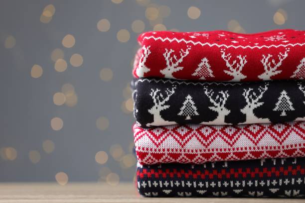 istock Stack of different Christmas sweaters on table against grey background with blurred lights. Space for text 1813651323