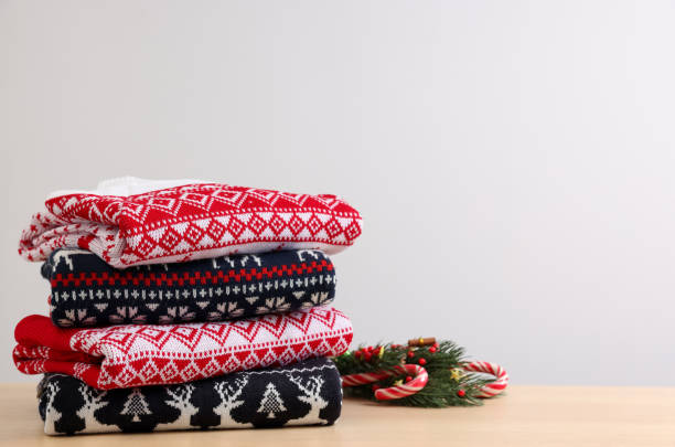 istock Stack of different Christmas sweaters and decor on table against light background. Space for text 1813651325