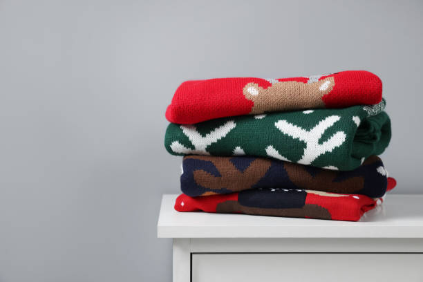 istock Different folded Christmas sweaters on chest of drawers against grey background. Space for text 1813651326
