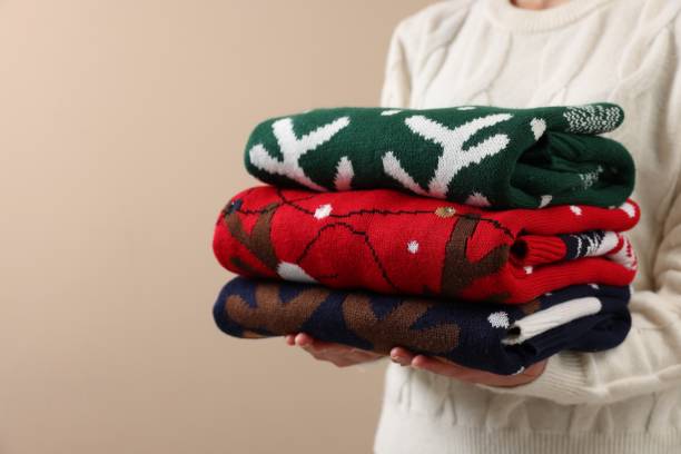 istock Woman holding stack of different Christmas sweaters on beige background, closeup. Space for text 1813651844