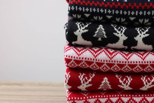 istock Stack of different Christmas sweaters on wooden table against light background, closeup. Space for text 1813651845