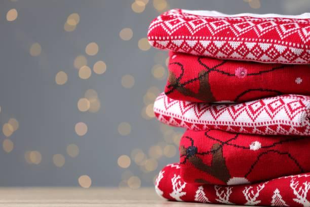 istock Stack of different Christmas sweaters on table against grey background with blurred lights. Space for text 1813651853