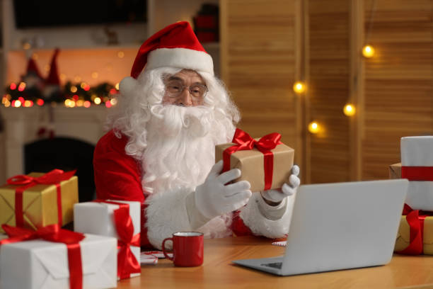 istock Santa Claus with Christmas gift using laptop at table in room 1813686746