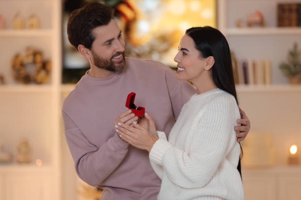 istock Making proposal. Man with engagement ring surprising his girlfriend at home on Christmas 1813698763