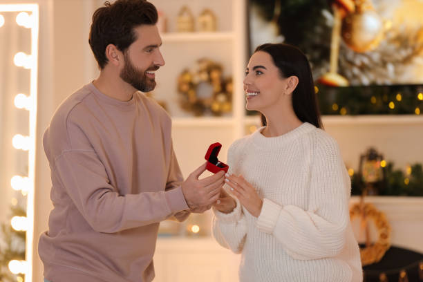 istock Making proposal. Man with engagement ring surprising his girlfriend at home on Christmas 1813699812