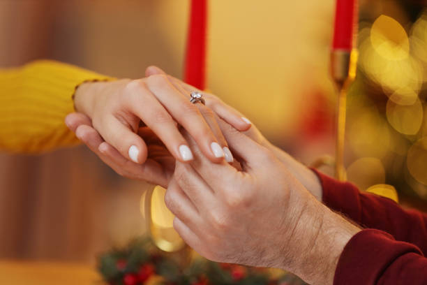 istock Making proposal. Man putting engagement ring on his girlfriend's finger at home on Christmas, closeup 1813699820