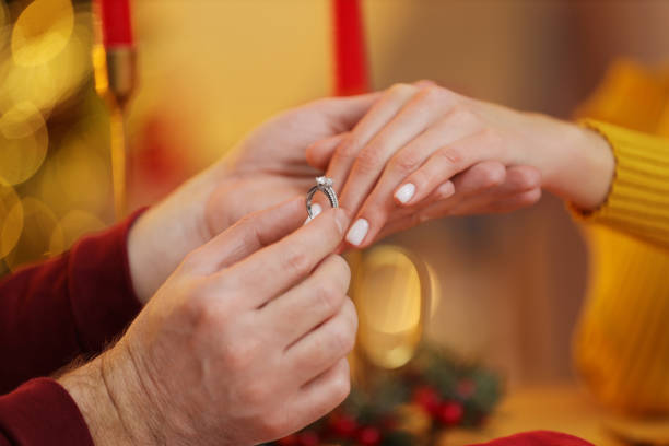 istock Making proposal. Man putting engagement ring on his girlfriend's finger at home on Christmas, closeup 1813700359