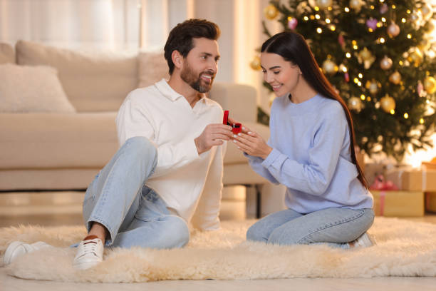 istock Man with engagement ring making proposal to his girlfriend at home on Christmas 1813700875
