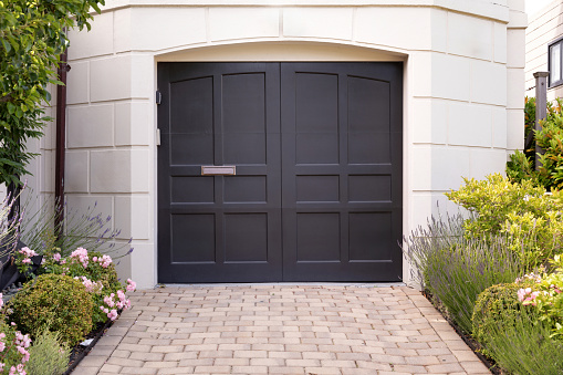 Front door that is black, there are two door with one mail slot, featuring brick paver stones, flowers and plants.