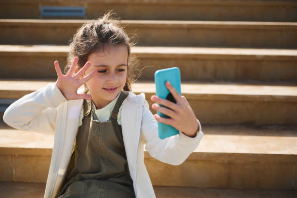 istock Caucasian girl using smartphone, online chatting, communication, smiling waving hello with hand, talking via video link, 1813770398