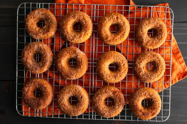 A dozen baked doughnuts covered in sugar with a mug of apple cider and cinnamon sticks