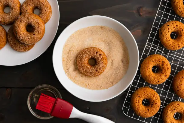 Baked doughnut in a shallow bowl full of organic cane sugar and ground cinnamon