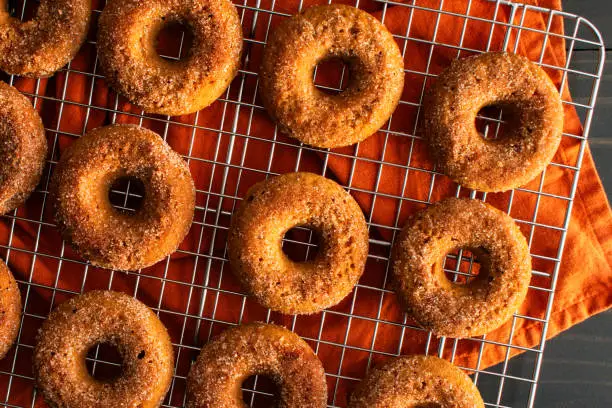 A dozen baked doughnuts covered in sugar with a mug of apple cider and cinnamon sticks