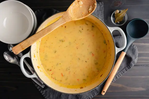 Creamy vegetable soup in a cast-iron pot with soup bowls and spoons on the side