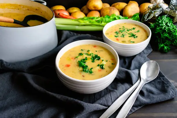 Bowls of vegetable soup with spoons next to a cast-iron Dutch oven and ladle