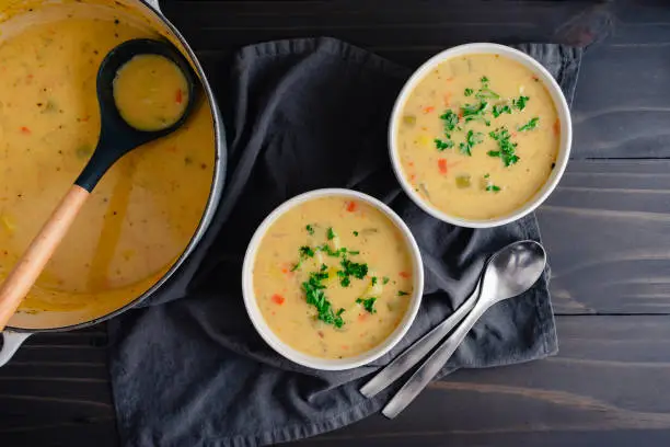 Bowls of vegetable soup with spoons next to a cast-iron Dutch oven and ladle