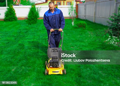 The man is working in the garden. Mowing grass with a lawn mower.